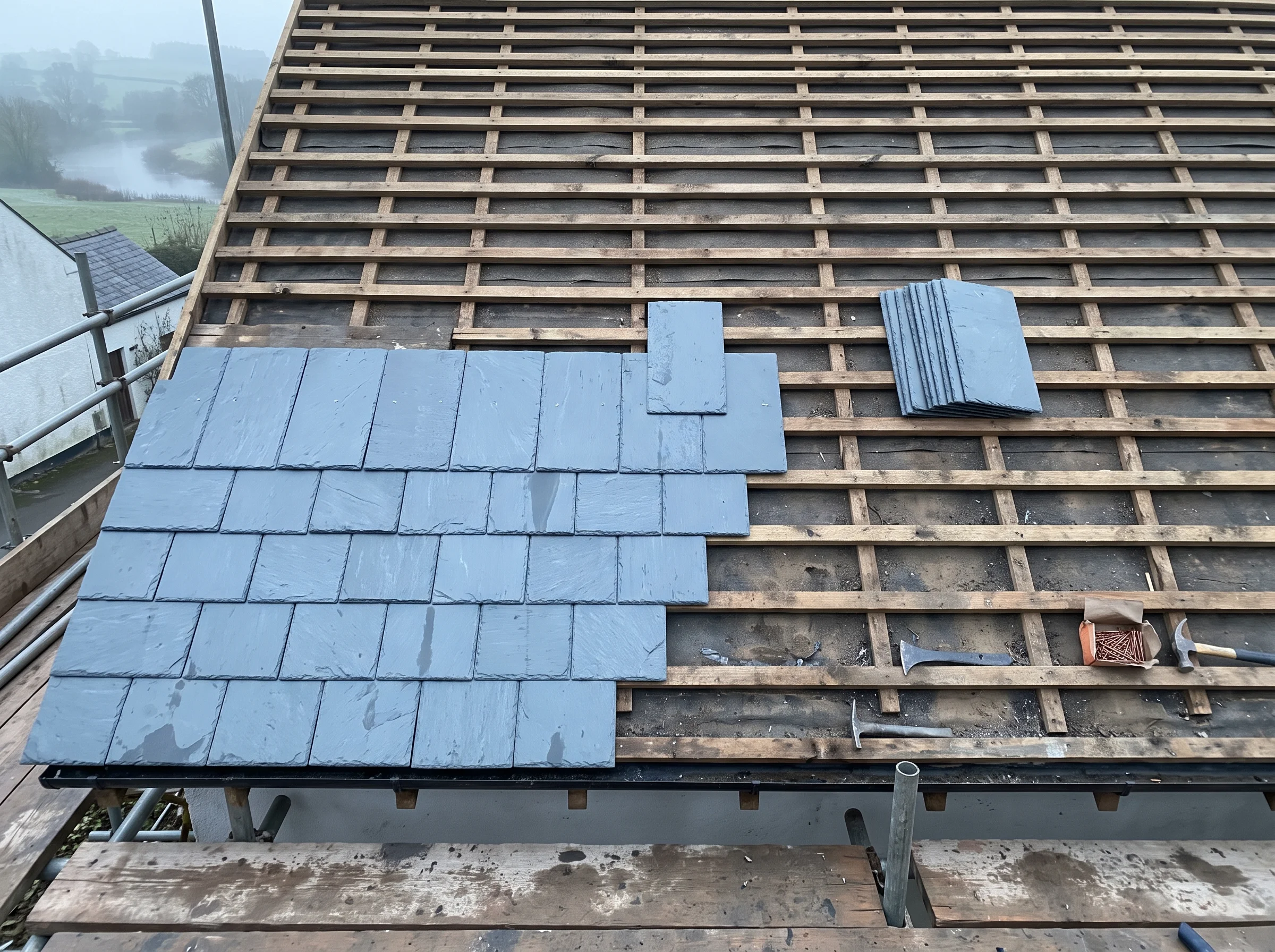 Stripped pitched roof showing bare battens with new Welsh slate courses laid part-way up